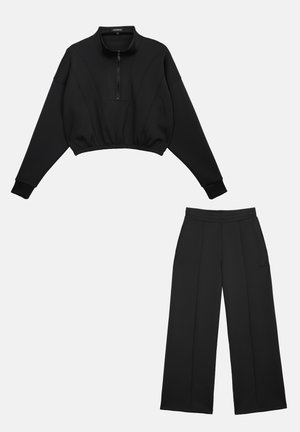 Ensemble noir deux pièces composé d'un pull court à manches longues avec fermeture éclair à l'avant et d'un pantalon large assorti sur fond blanc.