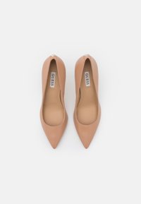 Escarpins nude en cuir verni avec bouts pointus et design minimaliste. Ils présentent une semelle intérieure avec le logo Guess et un accent à l'arrière du talon.