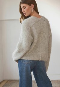 Light gray fuzzy sweater with a wide neckline and ribbed hem, paired with blue jeans featuring small metallic accents.