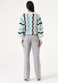 Geprint gebreid sweatshirt met golvende strepen in teal, beige en zwart. Gecombineerd met lichtgrijze high-waisted cargobroek met zakken.