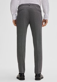Pantalons gris ajustés avec une texture lisse, une taille élastique et deux poches arrière, présentant des panneaux latéraux contrastants.