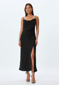 Zwarte satijnen maxi-jurk met een getailleerde silhoutte, een uitsnijding aan de zijkant en decoratieve knopen aan de linkerkant. Heeft dunne bandjes en een gladde textuur.