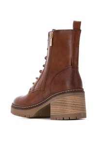 Botín de cuero marrón hasta el tobillo con cremallera lateral, cordones en la parte delantera, acentos texturizados y un tacón robusto y estriado. Suela de goma durable.