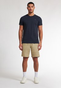 Marineblaue Baumwoll-T-Shirt mit kurzen Ärmeln und rundem Ausschnitt, kombiniert mit beigen Leinen-Shorts. Weiße Sneakers und gerippte Socken vervollständigen das Outfit.