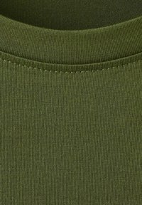 Detailný záber olivovo zelenej rebrovanej látky zobrazujúci okrúhly výstrih a precízne prešívanie pleteného odevu.