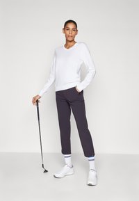 Suéter branco em V, calças cinza escuras com bolsos, ténis brancos e meias com detalhes azuis. Segurando um taco de golfe. Design simples, textura suave.