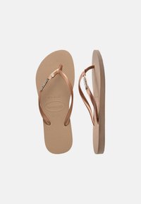 Beige flip-flops with textured soles and rose gold straps, featuring brand logo and decorative metallic accents on straps, shown front and side.