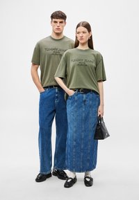 Tricouri verde măsliniu cu logo-ul „TOMMY JEANS”, pantaloni din denim cu croială largă și fustă lungă din denim; poșetă mică neagră și pantofi completează ținutele.