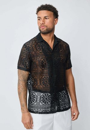 Chemise noire à manches courtes en dentelle complexe avec des motifs floraux, dotée d'un col et de boutons, au design semi-transparent et à la coupe décontractée.