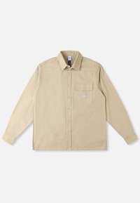 Maglia beige a maniche lunghe in tessuto di cotone, con colletto classico, chiusura con bottoni, taschino sul petto e patch del marchio sulla tasca.