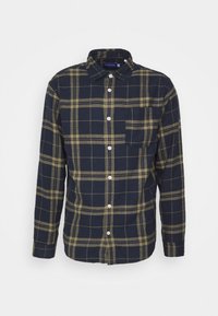 Camisa de franela a cuadros en azul marino y verde oliva con cuello abotonado, mangas largas y bolsillo frontal. Cuenta con botones blancos y una tela texturizada.