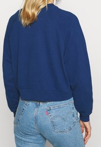 Felpa cropped blu navy con scollo rotondo e maniche raglan, abbinata a jeans in denim chiaro a vita alta.
