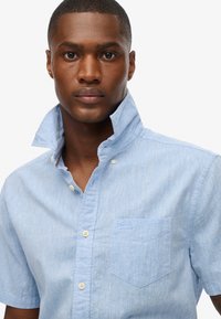 Niebieska lniana koszula z krótkim rękawem, z kołnierzykiem, kieszonką z przodu i zapięciem na guziki. Charakteryzuje się delikatną fakturą oraz logo na kieszeni.