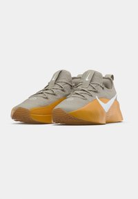 Chaussures de sport grises avec une tige texturée, une semelle en caoutchouc orange et des détails blancs en accent. Elles présentent une forme arrondie et un embout renforcé.