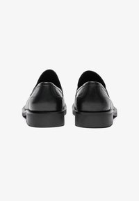 Zwarte leren instappers met een gladde afwerking, ronde neus en lage rubberen hak. Stiksels zichtbaar aan de achterkant en zijkanten.