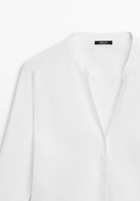 Wit overhemd met lange mouwen en kraag, voorzien van knopen, iets openstaande halslijn, textiellabel zichtbaar aan de binnenkant van de kraag.