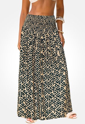 Frau trägt einen hoch taillierten, schwarz-beigen langen Rock mit geometrischem Muster, weißen Sandalen und Armbändern am rechten Arm.
