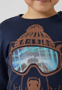 Granatowa koszula z długim rękawem z grafiką niedźwiedzia; posiada brązowe akcenty i żywy obraz zaśnieżonego krajobrazu w goglach niedźwiedzia.