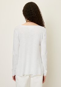 Ilgas rankoves, lengvas baltas viršus su apvaliu iškirpimu ir kreivu apačiu. Minkšta medžiaga su šiek tiek permatomu tekstūru.