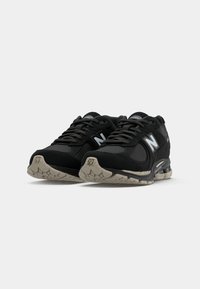 Black athletic shoes with mesh and synthetic upper, featuring a prominent white "N" logo, thick rubber sole, and textured accents.