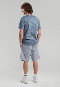 Light blue cotton t-shirt with white wave graphic and "WAVES" text on back, paired with gray shorts and white sneakers with green accents.