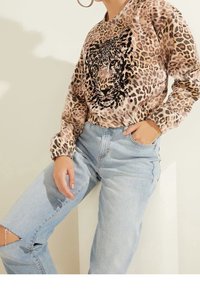 Sudadera de estampado de leopardo en beige con detalles en negro y un gráfico de tigre. Combinada con jeans rasgados de color azul claro. Tejido de mezcla de algodón.