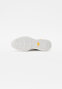 Light gray rubber outsole with a textured pattern, featuring a central yellow logo, designed for traction and durability.