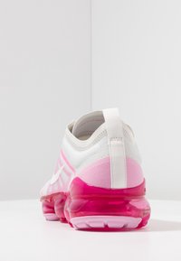Scarpa sportiva rosa e bianca con tomaia in rete, suola spessa e traslucida, e linguetta in tessuto. Presenta un motivo a zigzag sui lati.