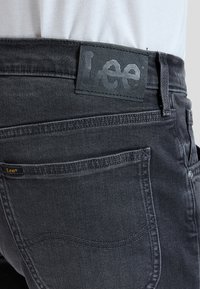Close-up af sort denim jeans bagpå med Lee mærke læderetiket og lille stofmærke, båret med skjorte stuvet ind.