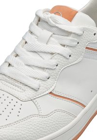Baskets blanches en cuir texturé, avec des lacets blancs et une subtile touche d'orange. L'embout comprend des perforations pour la respirabilité.
