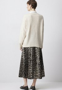 Maglione oversize color crema realizzato in morbido knit, abbinato a una gonna midi con stampa leopardata nera e beige, con orlo ampio e leggera texture.