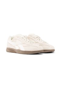 Baskets en daim beige avec des accents blancs, des détails perforés et une semelle en caoutchouc marron clair, dotées d'une fermeture à lacets plats et d'un bout arrondi.