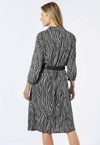Zwart-wit gestreepte jurk met een kraag, lange mouwen en een ceinture taille. Vloeiende stof met een golvende lijnontwerp.