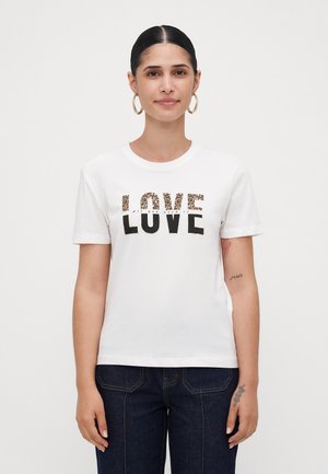 Woman with dark pulled-back hair wearing gold hoop earrings and a white T-shirt with "LOVE" in black and leopard print letters.