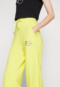 Gula sweatpants med sidfickor, dragsko i midjan och en silverhjärt-logotyp med "LOVE MOSCHINO" på vänster ben. Mjuk tyg.