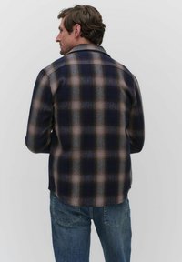 Rutigt flanellskjorta med mörk marinblå och jordnära toner, klassisk krage, långa ärmar och en avspänd passform med en lätt kurva vid fållen.