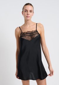 Abito slip in satin nero con dettagli in pizzo sul collo, caratterizzato da spalline sottili e regolabili e una consistenza morbida e liscia.