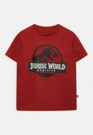 Rød t-shirt med korte ærmer med sort Jurassic World Dominion-logo med en T-Rex-silhuet i en cirkulær design midt på fronten.