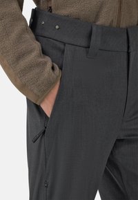 Harmaat housut, joissa on sileä pinta ja räätälöity istuvuus. Niissä on tasainen etuosa, sivutaskut ja vyötäröllä nappikiinnitys.