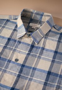 Button-up shirt featuring a blue and beige plaid pattern, made from a textured fabric with a collared neck and two blue buttons.