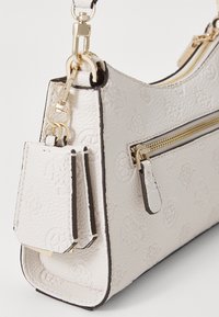 Borsa in pelle bianca con effetto goffrato, hardware dorato, tasca con zip e charm removibile. Presenta una finitura testurizzata e un rivestimento nero a contrasto.