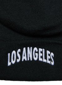 �Čierna pletená čiapka s bielym vyšitým textom "LOS ANGELES" na manžete. Text je v tučnom, veľkom písmene. Texturovaná tkanina.
