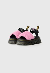 Svarte platå sandaler med rosa faux pelsremmer, med en teksturert svart såle og gule aksentremmer merket "A.A.M." med en stjernedetalj.