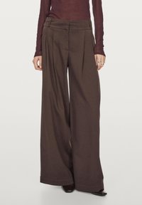 Brązowe spodnie typu wide-leg z kantami, wykonane z miękkiego materiału. Posiadają dopasowany pas i wykończenie na prosto. Noszone z dopasowanym topem.