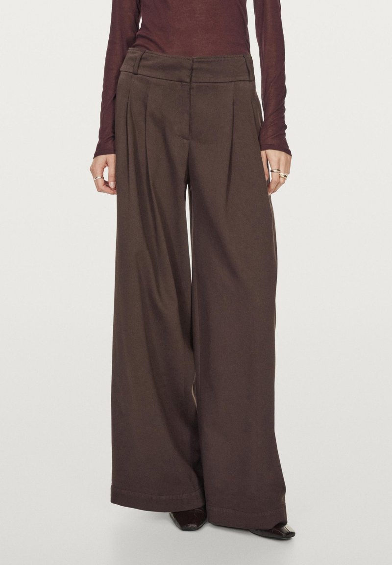 Hnědé kalhoty širokého střihu s záhyby, vyrobené z měkké látky. Mají upravený pas a čistý lem. Nosené s přiléhavým topem.