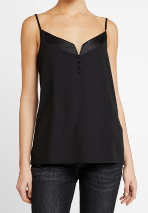 Kvinde iført sort ærmeløs V-hals top med fire knapper foran, kombineret med mørke jeans, vist fra nakke til hofter.