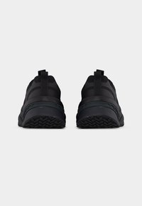 Ζεύγος μαύρα αθλητικά παπούτσια, ορατά από πίσω, με ανάγλυφες σόλες και θηλιές έλξης στη φτέρνα, σε απλό λευκό φόντο.