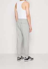 Pantaloni sportivi grigi con vestibilità affusolata, realizzati in tessuto morbido, caratterizzati da una tasca posteriore. Indossati con una canotta bianca e sneaker nere.