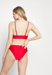 Conjunto de biquíni vermelho com textura canalizada, alças finas ajustáveis no top e calções de cintura alta com uma faixa lisa na cintura.