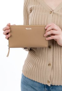 Isik beežist soonikkoes kardiganis hoiab mõlema käega rinnatsoonil tan värvi Tamarise tõmblukuga ümbrist.